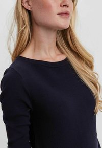 Pull en maille bleu marine avec un large col ras du cou, des manches longues et une texture côtelée, affichant un design ajusté sans détails supplémentaires.