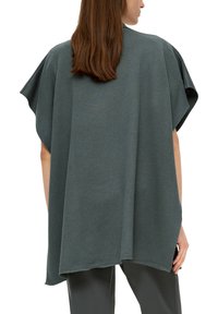 Overgroot, donkergroen poncho-vest gemaakt van zachte stof. Kenmerkt zich door brede mouwen en een relaxte pasvorm, met een langere achterkant voor extra flair.