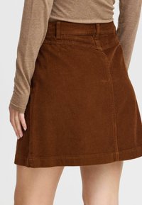 Jupe en velours côtelé brun avec des côtes verticales, dotée d'une taille ajustée et d'un ourlet droit. Design simple sans matériel ni motifs visibles.