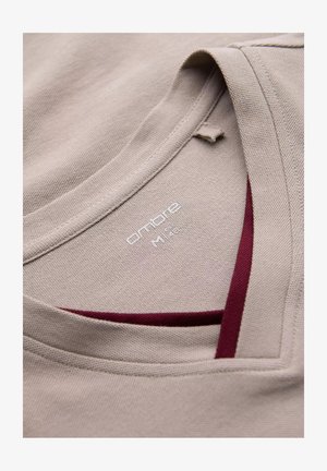 Beżowa koszulka z teksturowanej tkaniny, z dekoltem w serek i bordo akcentem przy wewnętrznej stronie dekoltu. Metka mówi "ombre M 14."