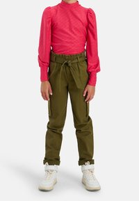 Top de manga larga rosa con un patrón texturizado, combinado con pantalones cargo verdes que tienen una cintura con cordón y bolsillos laterales. Zapatillas blancas completan el look.