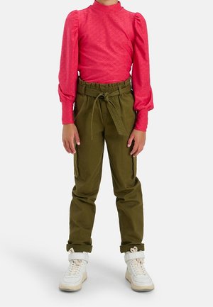 Top de manga larga rosa con un patrón texturizado, combinado con pantalones cargo verdes que tienen una cintura con cordón y bolsillos laterales. Zapatillas blancas completan el look.