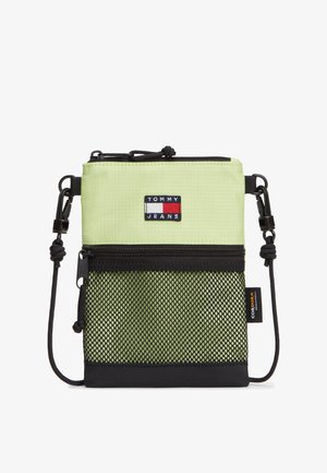 Pequeña bolsa bandolera de color verde claro y negro con bolsillo delantero de malla con cremallera, correa ajustable de cordón y parche con el logo de Tommy Jeans.