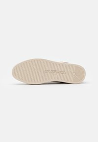 Fehér sneaker talp texturált gumiból, barázdákkal a tapadás érdekében, és egy logóval a sarok közelében, mely fel van domborítva. Lapfelszín, minimalista esztétika.