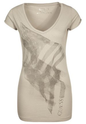 Beżowy damski T-shirt z dekoltem w serek, z abstrakcyjnym flagowym wzorem w odcieniach szarości oraz pionowym napisem "GUESS" blisko krawędzi.