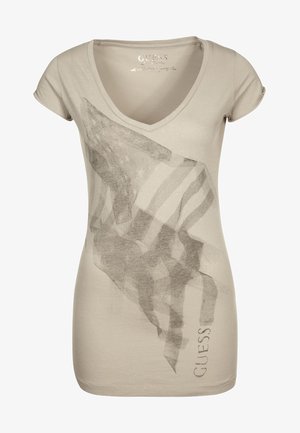 Beige Damen-T-Shirt mit V-Ausschnitt, bedruckt mit einem abstrakten Flaggen-Design in Graustufen und dem Schriftzug "GUESS" senkrecht nahe dem Saum.