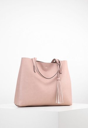 Sac cabas en cuir rose doux avec double poignée et un long détail en pampille, posé sur un socle blanc contre un fond uni.