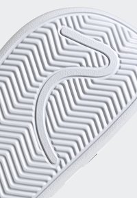 Suola di sneaker in gomma bianca con un motivo a spina di pesce testurizzato e una linea di accento liscia e curvata. Durevole e progettata per la trazione.