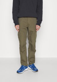 Olive cargo-byxor med flera fickor, figurnära design och lättviktsmaterial. Matchas med blå träningsskor med vita sulor.