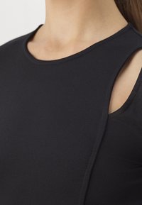 Black sleeveless top made of stretchy fabric, featuring a round neckline and cut-out detail at the shoulder for added design.