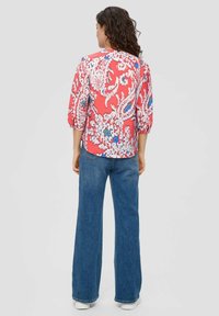 Rode bloes met driekwartmouwen, versierd met blauwe en witte paisley patronen, gecombineerd met high-waisted blauwe jeans.