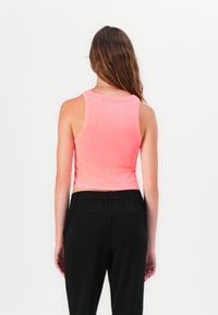 Bright pink cropped tank top with a ribbed texture and wide armholes, paired with black elastic-waist pants featuring back pockets.