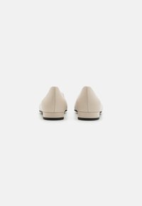 Scarpe slip-on beige con una texture liscia, tacco basso e punta arrotondata, dotate di una suola nera e design minimalista.