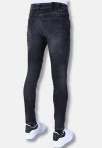Zwarte skinny jeans met een vervaagde afwerking, voorzien van een taille met middenhoogte en achterzakken. Gecombineerd met witte sneakers voor contrast.