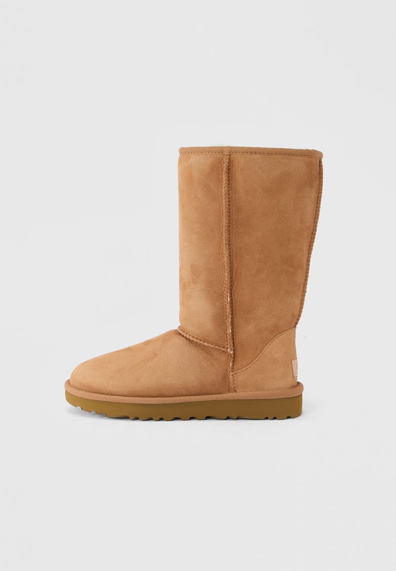 Hellbrauner Wildlederstiefel bis zur Mitte der Wade mit dicker Sohle und sichtbaren Nähten, von der Außenseite auf einem einfarbigen Hintergrund gezeigt.