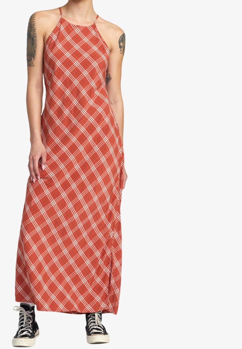 Robe longue rouge à carreaux blancs, design à col licou, fabriquée en tissu léger. Comprend une poche latérale et est associée à des baskets noires.