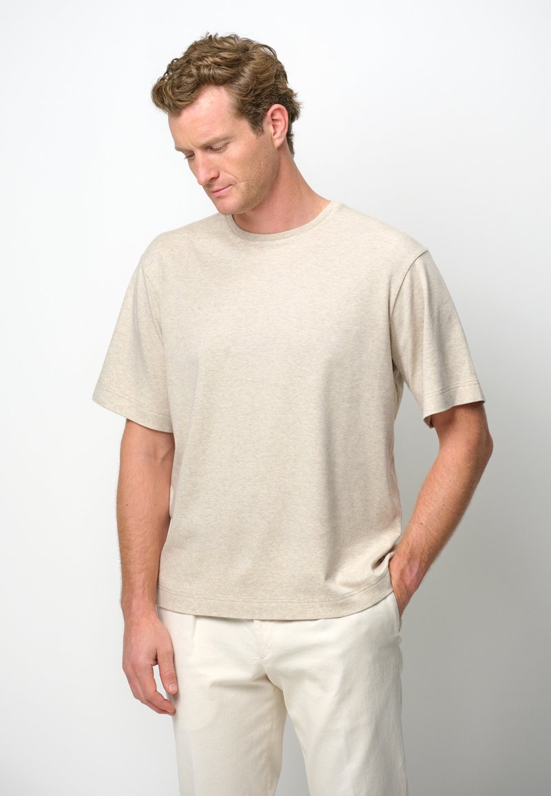 Beige bomull t-shirt med korta ärmar, rund halsringning och en avslappnad passform. Bärs med ljusa byxor, minimal textur.