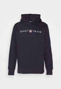 Sudadera azul marino con mangas largas, puños acanalados y texto frontal "GANT 1949" con el logo del escudo entre el texto.