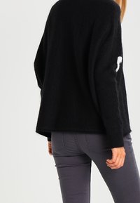 Pull noir en maille avec une coupe ample, doté d'un col rond et d'un accent blanc sur la manche. Associé à un pantalon gris ajusté.
