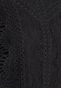 Tissu en dentelle noire avec des motifs floraux et tourbillonnants en boucle créant un design texturé et complexe.