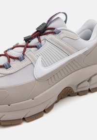 Svjetlosivi tenisice s teksturiranom gornjom, elastičnim crvenim i plavim vezicama te bijelim Nike logom. Imaju debeli potplat s smeškim gumenim gaznikom.