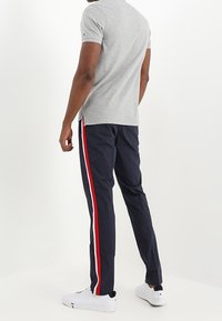 Grå kortärmad polotröja, marinblå byxor med vit-röda sidorieser, och vita sneakers. Minimalistisk design med atletisk passform.