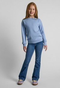 Ljusblå långärmad tröja med ribbade muddar, kombinerad med mörka utställda jeans och lila/bruna sneakers. Enkel, avslappnad outfit.