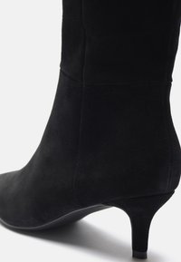 Bottine en daim noir à la forme effilée, avec un léger talon, une texture lisse et un design sans couture ; sans matériel visible ni accents.