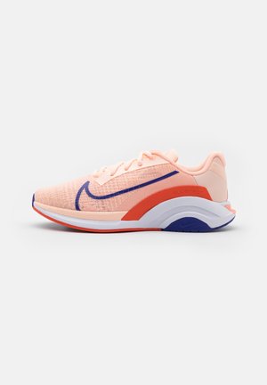 Hellrosa Sportschuh mit dunkelblauem Nike-Swoosh, rotem Mittelsohlenakzent, weißer Sohle und atmungsaktivem Mesh-Obermaterial, Seitenansicht.