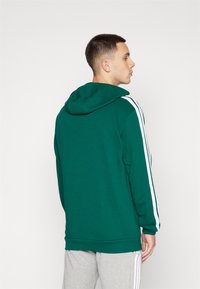 Grön hoodie med vita ränder på ärmarna, mjuk textur, avslappnad passform och en rymlig huva. Enkel design, ribbad nederkant och cuffar.