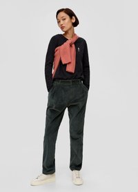 Ciemna koszula z długim rękawem z małym haftem, w zestawieniu z ciemnozielonymi spodniami z kordurowej tkaniny i jasnoczerwoną swetrem przewiązanym na ramionach.