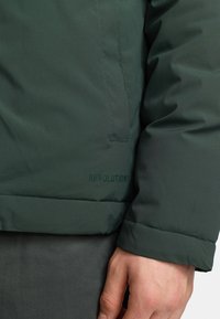 Dark green padded jacket featuring a smooth exterior, elastic cuffs, and a hem with an embroidered "REVOLUTION" logo.