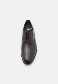 Zapato de vestir de cuero marrón con un acabado suave, punta redonda, cuatro ojales y cordones oscuros. Presenta un sutil logo en relieve en el lateral.