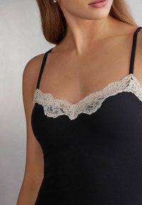 Camisola nera a coste con spalline sottili e un bordo in pizzo color beige chiaro lungo lo scollo, che mette in risalto i delicati dettagli tessili.