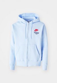 Sudadera con cremallera en azul claro, fabricada en una mezcla de algodón. Cuenta con un bolsillo frontal tipo canguro, puños acanalados y un logo de Nike en rojo con el texto "SOLO PERSONAL AUTORIZADO".