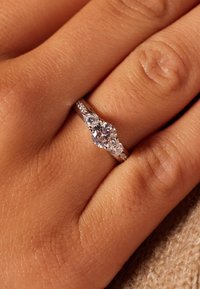 Drie-stenen verlovingsring met een zilveren band, met een centrale ronde diamant en kleinere zijdiamanten, textuur van een handachtergrond.