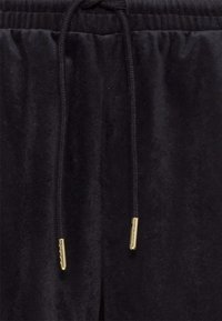 Zbliżenie czarnych welurowych spodni z elastycznym pasem i czarnymi sznurkami z złotymi metalowymi zakończeniami.