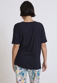 Svart kortärmad t-shirt med avslappnad passform, mjukt tyg och bred halsringning, i kombination med byxor i färgglatt blommönster.