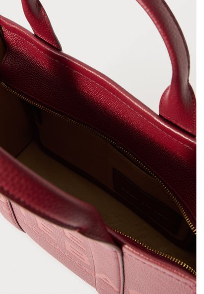 Odprta rdeča usnjena torbica z zlatim zadrgo in bež tekstilno notranjostjo z notranjim žepom.