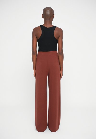 Top negro sin mangas combinado con pantalones anchos de color óxido, que muestran una textura suave y un ajuste relajado, vistos desde atrás.