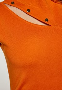 Top tricotat cu nervuri portocalii, având un design distinctiv cu decupaj aproape de guler, accentuat cu nasturi aurii cu clips.