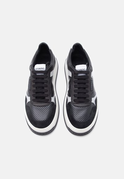 Paire de baskets perforées noires et blanches avec lacets noirs, semelles intermédiaires blanches et marque "ICEBERG" sur la languette et les côtés.