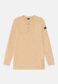 Camisa henley de manga longa em tom beige, feita de um tecido suave, com três botões na frente, um decote redondo e um logótipo na manga esquerda.
