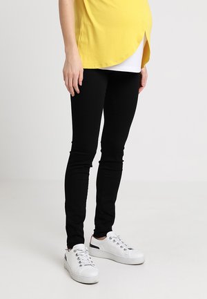 Leggings pretos feitos de material elástico, combinados com uma camisa amarela larga e ténis brancos. Apresentam uma textura suave e um design ajustado.