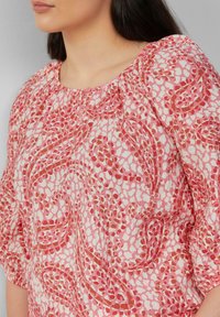 Vloeiende roze blouse met een subtiel bloemmotief, ronde halslijn en geplooide details op de mouwen. Gemaakt van lichtgewicht stof.