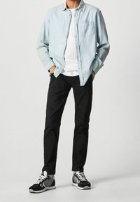 Camicia button-up azzurro chiaro, t-shirt bianca sotto, pantaloni neri e sneakers bianche e nere con dettagli grigi. Stile casual, vestibilità rilassata.