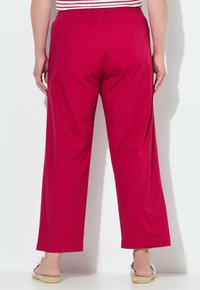 Rote, weit geschnittene Hosen mit elastischem Bund; flache Nähte und Aufschläge am Saum. Getragen mit einem gestreiften Oberteil und Espadrilles.