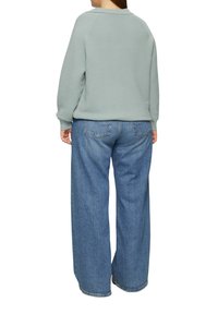 Helles grünes geripptes Sweatshirt mit Rundhalsausschnitt, kombiniert mit hochgeschnittenen, weit geschnittenen blauen Jeans aus Denim. Sichtbare Nähte und lässige Passform.