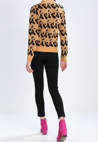 Gebreide trui in tan met zwart dierenprint, lange mouwen en ribbelmanchetten; gecombineerd met zwarte skinny jeans en roze enkellaarsjes.