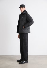 Svart puffjakke med hette og glidelås, med en boksaktig design. Kombinert med svarte cargo-bukser og stilige svarte sko.